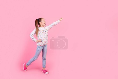 Foto de tamaño completo de colegiala positiva vestida puño jersey punteado dirigir espacio vacío mirar a la venta aislado en el fondo de color rosa.