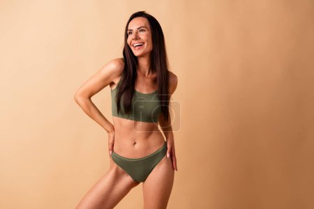 Fotoporträt von attraktiven jungen Frau berühren Taille hübsches Modell keine Retusche tragen trendige khaki Dessous isoliert auf beige Hintergrund.