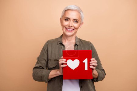 Portrait photo of cheerful influencer woman wearing khaki shirt holding red button subscription isolated on beige color background.
