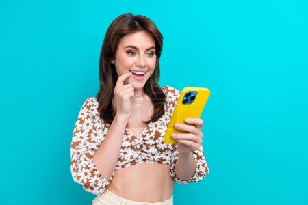 Portrait of cute beautiful young lady brunette hair touch cheek looking at her bank account in smartphone isolated on cyan color background.