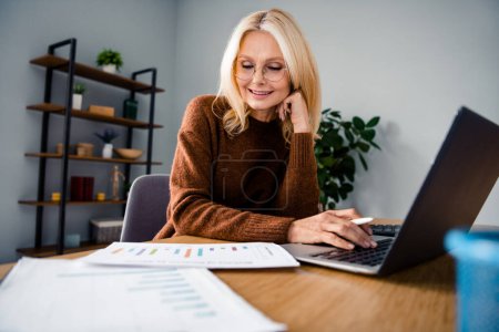 Photo of startup projects manager blond hair mature successful woman in brown sweater sitting desktop paperwork with money spends company.