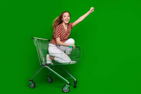 Foto de longitud completa de funky alegre adolescente vestido impresión blusa sentarse en el carro levantando puño divertirse aislado sobre fondo de color verde.