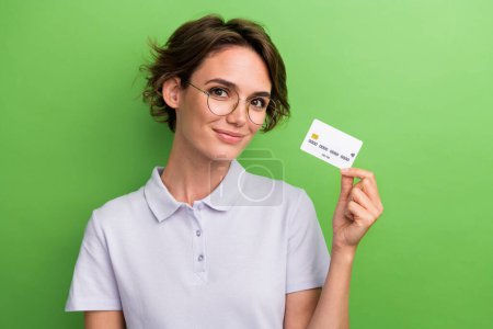 Photo of adorable lovely girl wear stylish clothes hand demonstrate plastic bank card isolated on green color background.