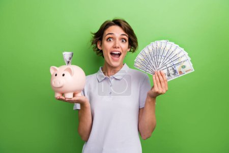 Photo of overjoyed girl hold piggy bank cash dollars rejoice wealth luxury future life isolated on green color background.