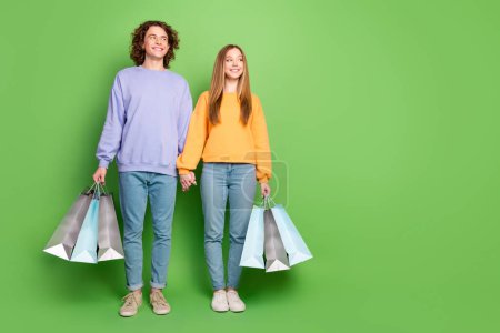 Retrato de tamaño completo de dos personas alegres sostienen las bolsas de la tienda de armas parecen espacio vacío anuncio aislado en el fondo de color verde.