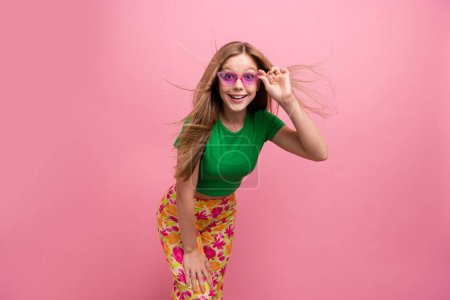 Foto retrato de encantadora chica adolescente toque sunglass compras posando ropa de moda ropa verde aislado en el fondo de color rosa.