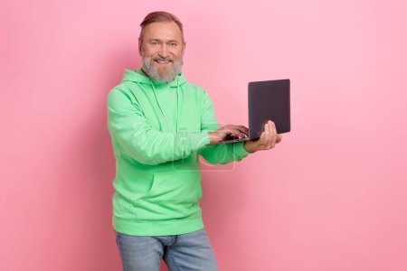 Photo of cheerful positive guy dressed green hoodie chatting apple samsung device empty space isolated pink color background.