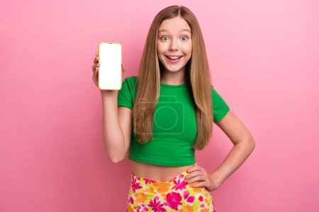 Foto von entzückenden schönen Mädchen tragen grüne trendige Kleidung Hand halten Telefonbildschirm leeren Raum isoliert auf rosa Hintergrund.
