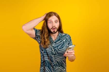 Photo of impressed positive guy wear print shirt reading news modern device isolated yellow color background.