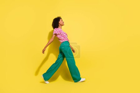 Perfil de cuerpo completo retrato de alegre hermosa dama caminando espacio vacío aislado sobre fondo de color amarillo.