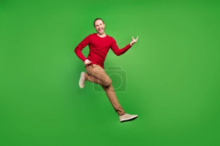 Full size photo of handsome funny man dressed red pullover brown pants jumping show rock symbol isolated on green color background.