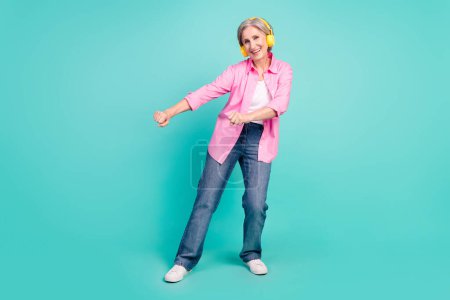 Full body length photo pensioner woman in pink shirt dancing boogie woogie listen music earphones isolated on blue color background.
