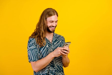 Photo of positive good mood guy wear print shirt communicating modern device empty space isolated yellow color background.