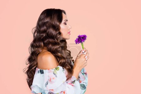 Close up half face profile side view photo of curly brunette person hold small purple bouquet of flowers in hand and breathe in their smell isolated on vivid turquoise background.