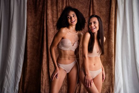 Studio photo of seductive smiling ladies dressed lingerie no filter skin tacking photos laughing isolated natural day light linen textile background.