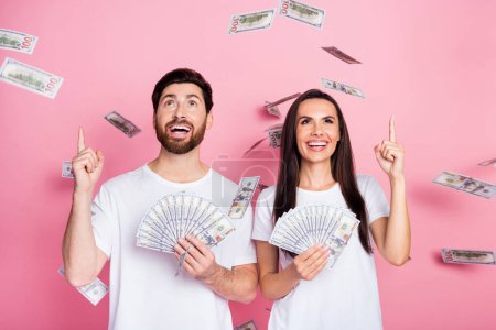 Photo portrait of lovely young couple hold money fan point look up vide espace porter tenue blanche à la mode isolé sur fond de couleur rose.