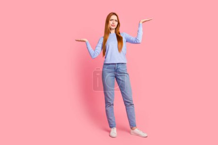 Full length photo of confused puzzled girl wear blue pullover palms hold similar objects empty space isolated on pink color background.