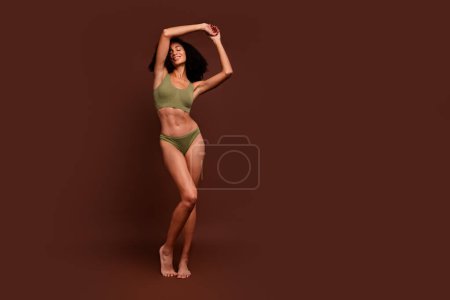 No filter full length photo of tender cute girl with raised hands promoting khaki lingerie empty space isolated on brown color background.