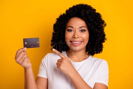 Photo of pleasant nice girlish woman with chevelure wear white t-shirt indicating at credit card isolated on yellow color background.