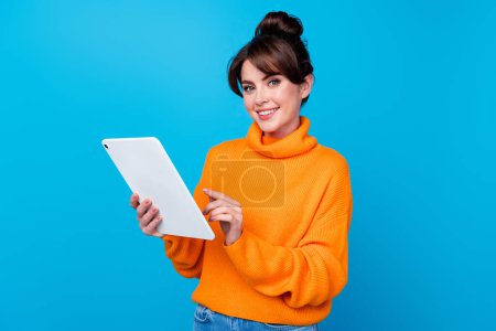 Photo of positive adorable woman dressed orange sweater texting messages modern device isolated blue color background.