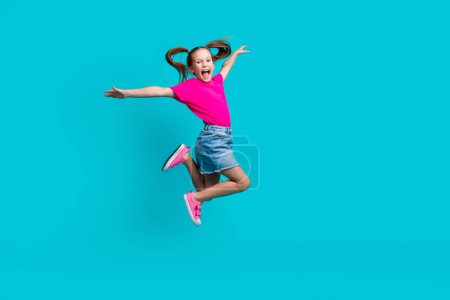 Full length photo of carefree cute flying girl wear stylish t-shirt denim skirt hold arms like wings isolated on teal color background.