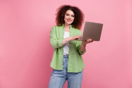 Photo portrait of lovely young lady hold netbook typing email dressed stylish green garment isolated on pink color background.