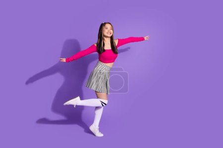 Full body photo of carefree cute schoolgirl wear crop top plaid skirt long socks holding arms like wings isolated on violet background.