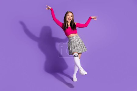 Full body photo of overjoyed funky schoolgirl wear crop top plaid skirt long socks having fun dancing isolated on violet background.