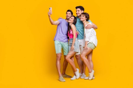 Foto de tamaño completo de cuatro compañeros se divierten juntos hacer selfie en gadget de células inteligentes aislado fondo de color vívido.