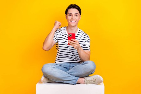 Photo de heureux heureux gars habillé rayé t-shirt gagnant jeu dispositif moderne isolé fond de couleur jaune.
