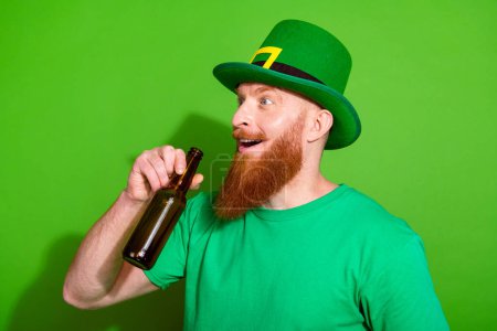 Profile portrait of astonished funky guy drink beer look empty space isolated on green color background.