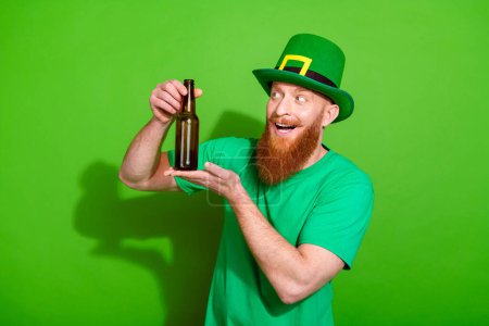 Photo of handsome charismatic young man arms hold showing glass beer bottle isolated on green color background.