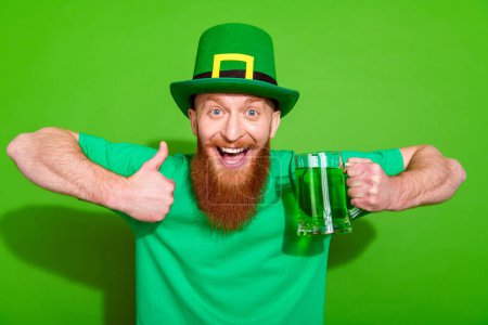 Foto von aufgeregten gutaussehenden Kerl halten Bier Ginger Ale Becher zeigen Daumen nach oben Zustimmung isoliert auf grünem Hintergrund.