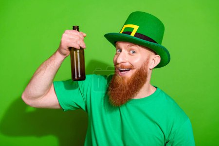 Photo of nice positive young man have good mood arm hold glass beer bottle isolated on green color background.