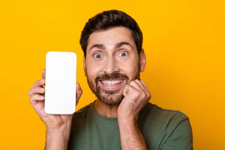 Photo portrait of attractive young man excited hold device touch cheek dressed stylish khaki clothes isolated on yellow color background.