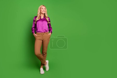 Full length photo of dreamy thoughtful woman wear violet shirt looking empty space isolated green color background.