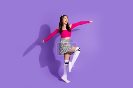 Full size photo of japanise girl dressed pink top checkered skirt stand on one leg look at sale empty space isolated on purple background.