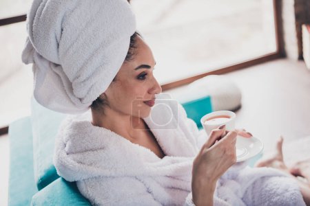 Portrait photo de jolie jeune femme assise canapé profiter tenir boire thé tasse tête enveloppé serviette habillée peignoir de bain intérieur profiter week-end.