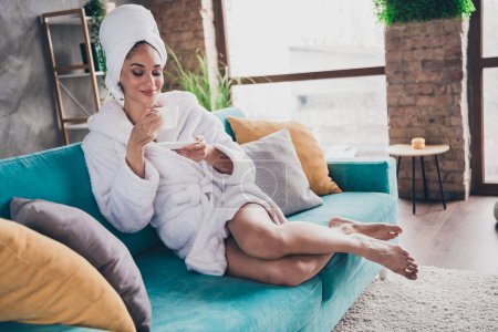Portrait photo de jolie jeune fille assise canapé boire thé tenir tasse tête enveloppée serviette habillée peignoir beauté routine concept maison.
