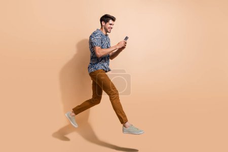 Full body length photo of professional content maker running with apple iphone 15 going post more videos isolated on beige color background.