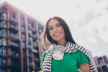 Portrait of beautiful brunette lady with beaming smile like sunny weather near city buildings outdoors on residential complex background.