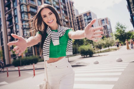 Photo of young friendly woman hugs wear green t shirt white pants greetings walking in good weather outdoors city residential complex.