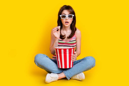 Ganzkörperfoto von erstaunten Mädchen tragen Strickpanzer in 3D-Brille halten Popcorn starrt auf Thriller-Film isoliert auf gelbem Hintergrund.