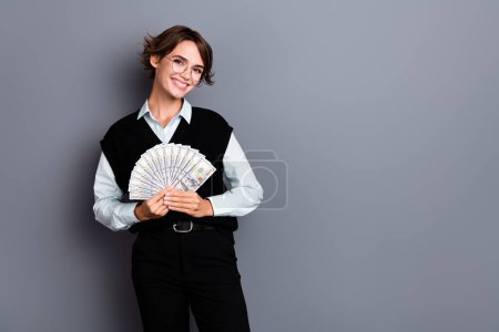 Foto von wunderschönen fröhlichen Dame tragen stilvolle schwarze Kleidung halten Geld Werbung Kreditbank isoliert auf grauem Hintergrund.