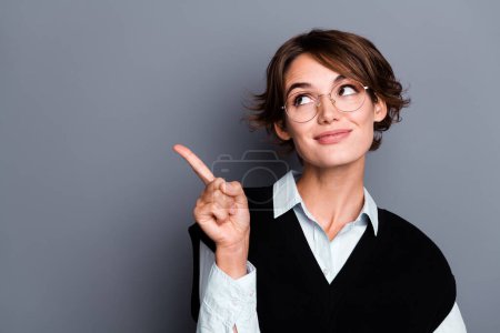 Photo of smart dreamy lady assistant dressed black vest eyewear looking pointing finger empty space isolated grey color background.