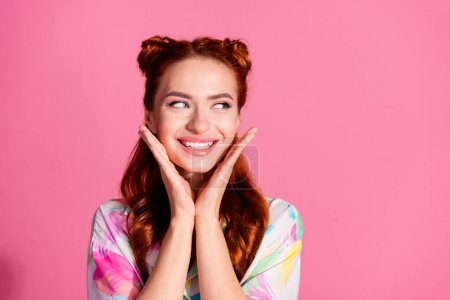 Photo of nice girl with redhair tails dressed colorful blouse look empty space offer hands on cheeks isolated on pink color background.