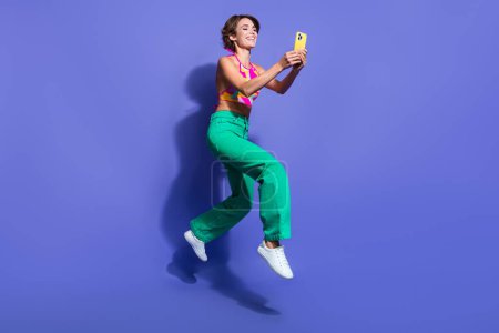 Ganzkörperfoto von jungen Hipster lustige Dame springen mit Smartphone hält Smartphone isoliert auf violettem Hintergrund.