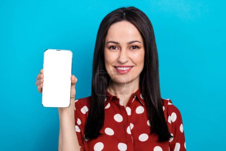 Foto-Porträt der attraktiven Frau halten Gadget-Show weißen Bildschirm gekleidet stilvolle gepunktete rote Kleidung isoliert auf blauem Hintergrund.