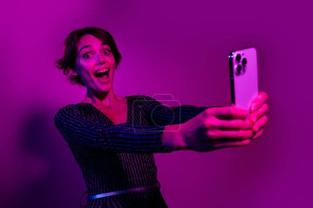 Photo portrait of attractive young woman hold excited gadget dressed stylish overall clothes isolated on neon light pink color background.