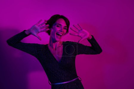 Photo portrait of attractive young woman raise hands dancing dressed stylish overall clothes isolated on neon light pink color background.
